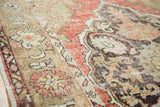 Distressed vintage Oushak rug detail, with faded cinnabar red, charcoal, and beige floral motifs.