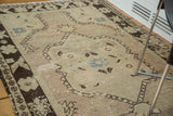 Distressed vintage Oushak rug with faded ivory field, chocolate brown patterns, and denim blue accents.