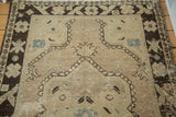 Distressed beige field with dark brown curvilinear medallion elements and faded blue motifs.
