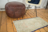 Faded beige Oushak rug with subtle peach and sea foam green medallion, purple selvedges.