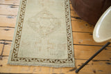 Distressed Turkish Oushak rug corner, subtle beige field, bronze geometric border, and fringe.