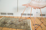 Vintage European rug with faded floral medallions and bubbly geometric border, under a chair.