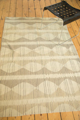 Hand-woven modern Kilim rug showing ivory, beige, and grey alternating diamond-shape patterns.