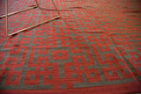Close-up of modern hand woven kilim with repeating red and charcoal knot pattern.