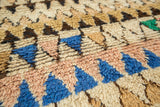 Close-up of plush Moroccan rug pile with bold blue, blush, and ivory geometric pattern.