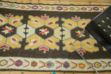 Distressed Turkish Kilim detail: geometric yellow, blue, ivory medallions on brown, with stylized border.