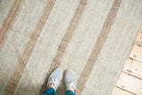 Feet on a simplistic, modern Turkish kilim rug with light grey and bronze stripes.