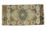 Vintage Oushak runner with ornate medallion, checkered corners, faded peach, green, and brown tones.