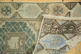 Folded vintage Oushak rug runner corner, displaying faded green, blue, brown geometric motifs, and fringe.