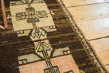 Oushak rug's geometric square medallions, arrows in dark brown, faded blush, and ivory.