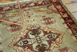 Textured view of distressed Oushak rug with intricate quatrefoil medallion in muted green and red.