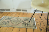 Faded blush, sage, and charcoal splayed floral and planter motifs on distressed Oushak runner.
