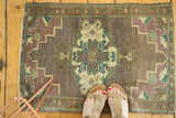 Oushak rug mat corner, mauve and pistachio spandrel motif, visible fringe.