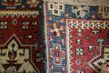 Hand-knotted pile showing small geometric patterns, cherry red, blue, and charcoal edge.