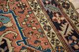Textured detail of vintage Heriz rug with geometric main border, floral elements, and brick red field.