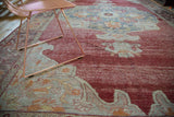 Distressed crimson Oushak carpet with faded cloudband pennant motifs.