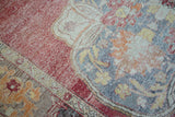 Distressed Oushak carpet detail, highlighting worn pile, crimson, tangerine, and soft blue colors.