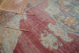Distressed crimson red Oushak rug with ivory and saffron curvilinear patterns.