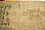 Beige Oushak rug runner's irregular weave, central medallion, tendrils, and charcoal border.