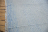 Minimalist Dhurrie rug texture, pale blue and ivory tones, with fringed edge.
