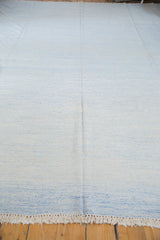 Close-up of hand woven Dhurrie carpet fringe and subtle ivory blue flatweave texture.