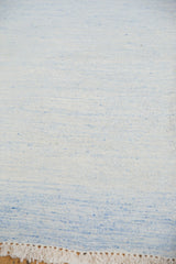 Dhurrie carpet's flat woven texture with subtle ivory and pale powder blue tones, plus fringe.
