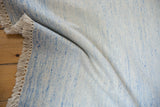 Textured hand woven Dhurrie rug, revealing minimalist pale blue and ivory weave and fringe.