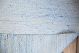 Minimalist hand-woven Dhurrie carpet edge revealing pale blue and ivory flatweave texture.