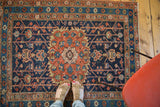 Distressed decorative corner of a Heriz rug, featuring geometric field patterns and floral borders in indigo and madder red.
