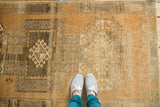 A person's feet on the vintage Oushak rug's distressed copper and bronze field.