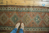 Vintage Heriz runner displaying repeating dark copper red and dark teal diamond pattern.