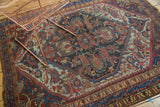 Distressed antique Qashqai rug's central hexagonal medallion, splayed floral motifs, and time-softened colors.