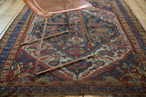 Distressed pile, tattered end, and intricate splayed floral motifs of an antique Qashqai rug.