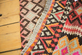 Contrasting geometric patterns on vintage Kilim rug edge with charcoal, blush, orange, and pale green.