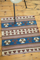 Hand woven geometric Kilim mat showing blue, ivory, brown, and blush patterns with fringe.