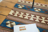 Hand-woven Kilim with geometric pinwheel and triangle patterns in blue, brown, and ivory.
