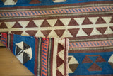 Kilim rug's folded corner reveals geometric pinwheel, triangular patterns; blue, ivory, brown, blush.