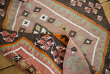 Irregular hand-woven texture of a vintage Turkish Kilim rug with plum, charcoal, and orange.