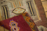 Folded corner of vintage Turkish Kilim rug with geometric red, purple, and orange motifs.