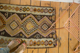 Corner view of a vintage geometric Kilim rug, with irregular weave and varied diamond patterns.