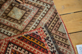 Folded view of hand woven Turkish Kilim rug, showing geometric diamond patterns, fringe, and red motifs.