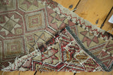 Jijim rug mat's irregular weave, faded red, brown diamonds, and visible tattered side.