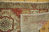 Folded corner of distressed Oushak runner revealing rich red pile, fringe, and hand-knotted foundation.