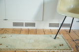 Vintage Oushak rug detail: faded celadon and sand tones, wave motif border, and fringe.