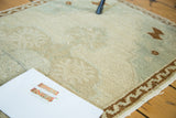 Faded beige and celadon pile of vintage Oushak rug, showing chocolate brown wave motif border.