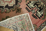 Folded corner of vintage Oushak rug revealing peach pink pile, dark pattern, and secure fringe.