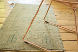 Distressed sand and beige Oushak rug surface with faded forest green outlines and even wear.