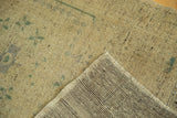 Distressed vintage Oushak rug's folded corner reveals soft sand pile, subtle green motifs, and woven reverse.