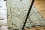 Angled view of vintage Oushak runner with pale celadon green, ivory, and charcoal brown floral motifs.