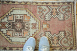 Vintage Oushak rug mat with distressed blush and sand geometric patterns, blue shoes.